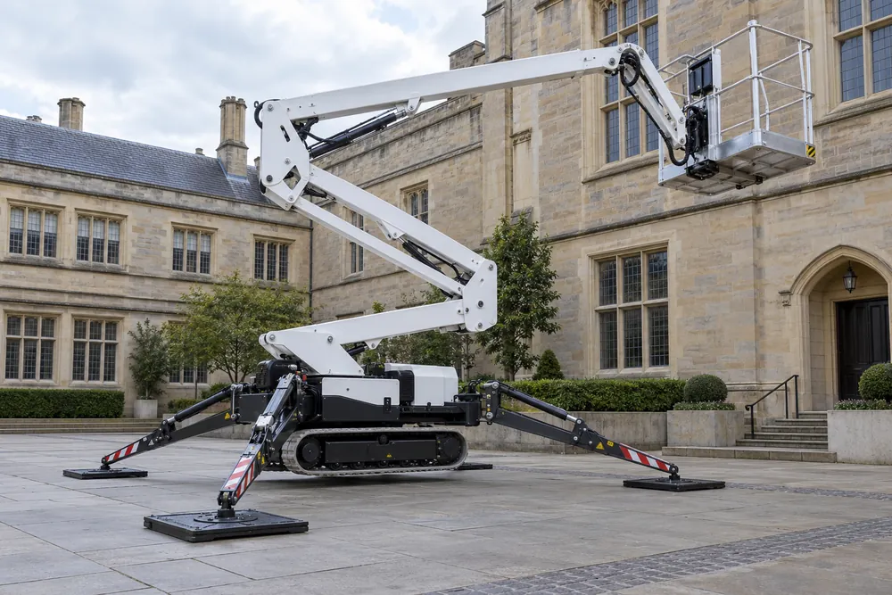 Tracked spider lift supported on extended stabilisers in a paved courtyard